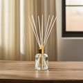 Reed diffuser with wooden sticks in a clear bottle on a wooden surface.